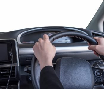 Hand holding steering wheel in modern private car with blank white windshield